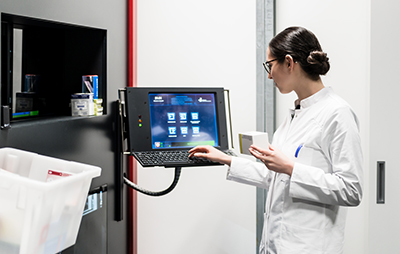 Female pharmacist standing in front of computer at pill dispensing machine